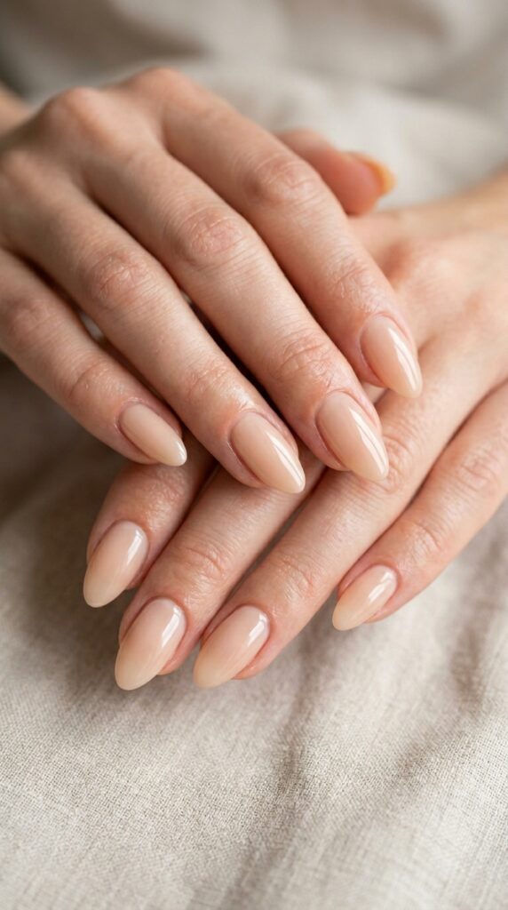 Hands with barely-there glossy nude nail polish featuring subtle pale color and brilliant finish without additional design elements emphasizing nail quality and elegant simplicity for refined minimalist summer manicure






