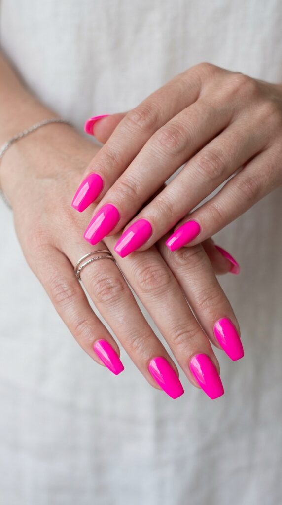 Hands with electric pink neon nail polish in solid full-coverage application showing vibrant fluorescent hot pink manicure with glossy finish for bold summer statement.