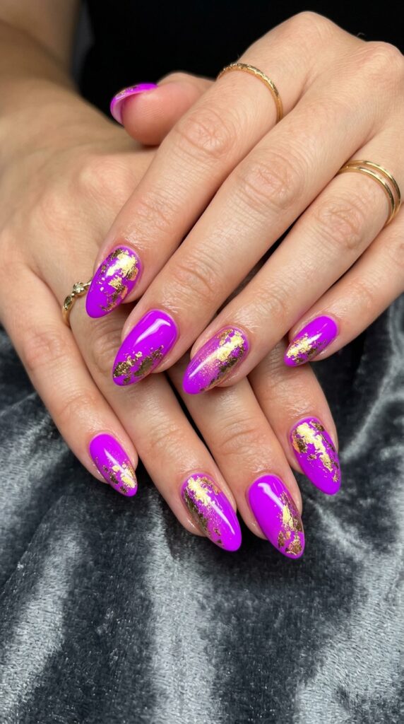 Hands with electric purple neon nail polish featuring layered gold foil accents creating glamorous metallic shimmer effect for luxurious bold summer manicure design






