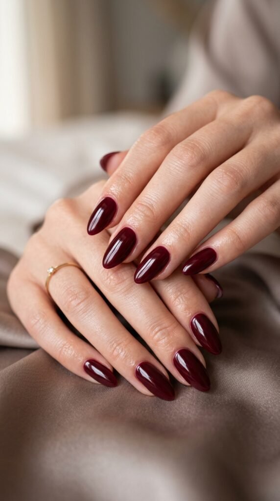 Close-up of burgundy gloss nails with deep red tones, shiny finish, and an elegant fall aesthetic