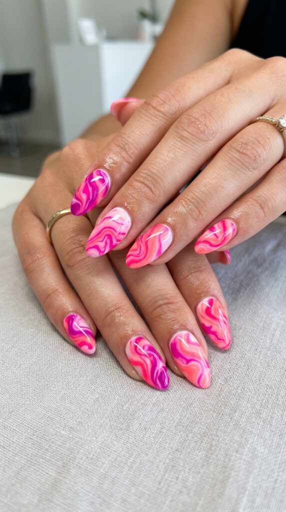 Hands with hot pink neon marble pattern created using multiple fluorescent pink shades in swirled water marble effect for sophisticated artistic summer manicure design







