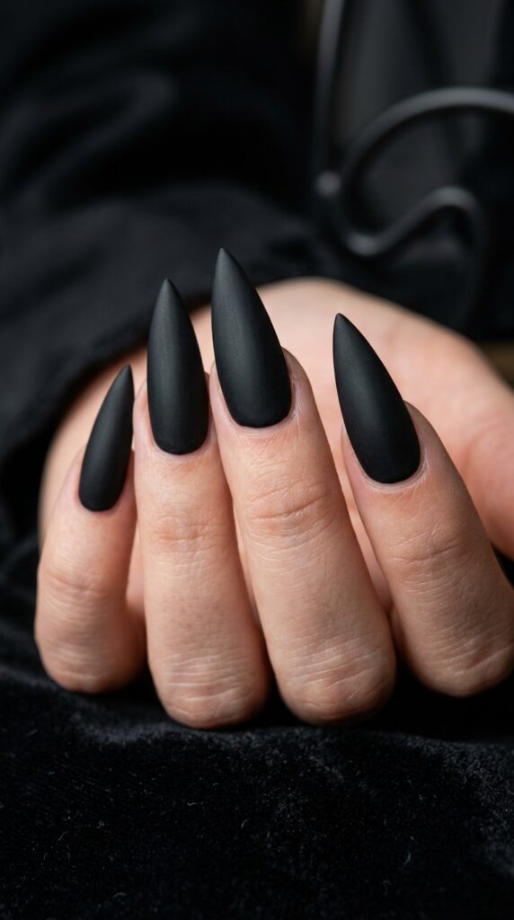 Matte black stiletto nails with a sharp pointed shape, smooth non-glossy finish, and a bold edgy aesthetic