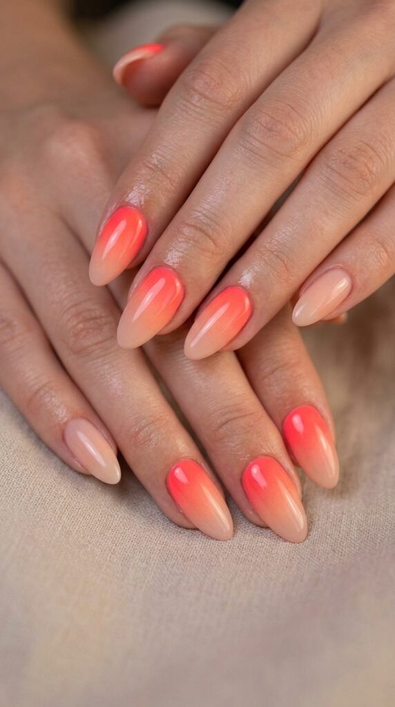Hands with neon coral gradient fading to nude at tips showing sophisticated transition from vibrant fluorescent base to sheer delicate tips for elegant summer manicure.