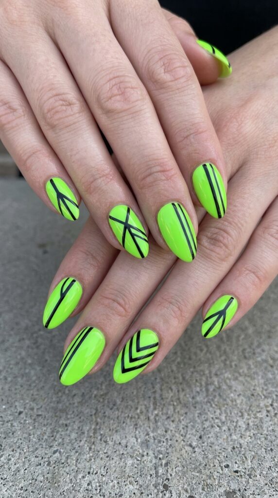 Hands with lime green neon base nail polish featuring bold black accent lines and geometric patterns creating striking contrast for modern bold summer design.