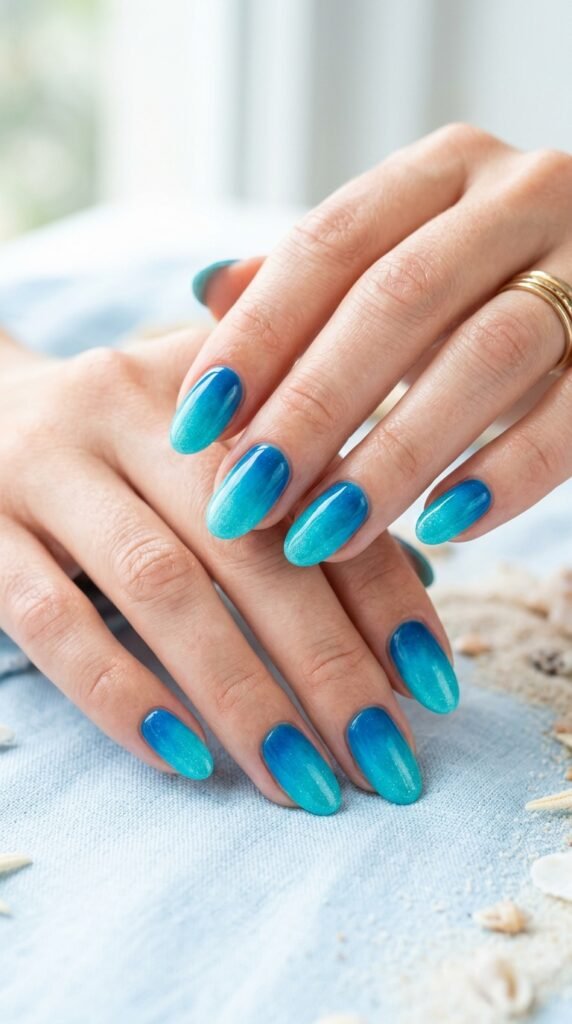 Ocean blue to turquoise ombre gradient nails with wave-like color transition from deep blue base to bright turquoise tips for tropical summer nail art.