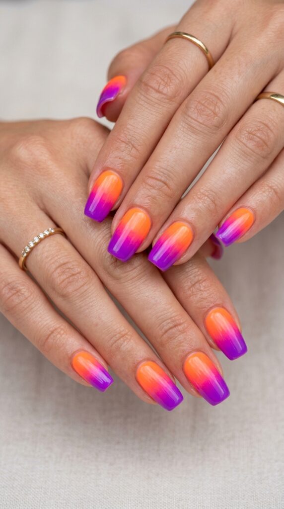 Hands with neon orange to purple gradient ombre nail design showing smooth fluorescent color transition from base to tips for vibrant summer neon manicure.