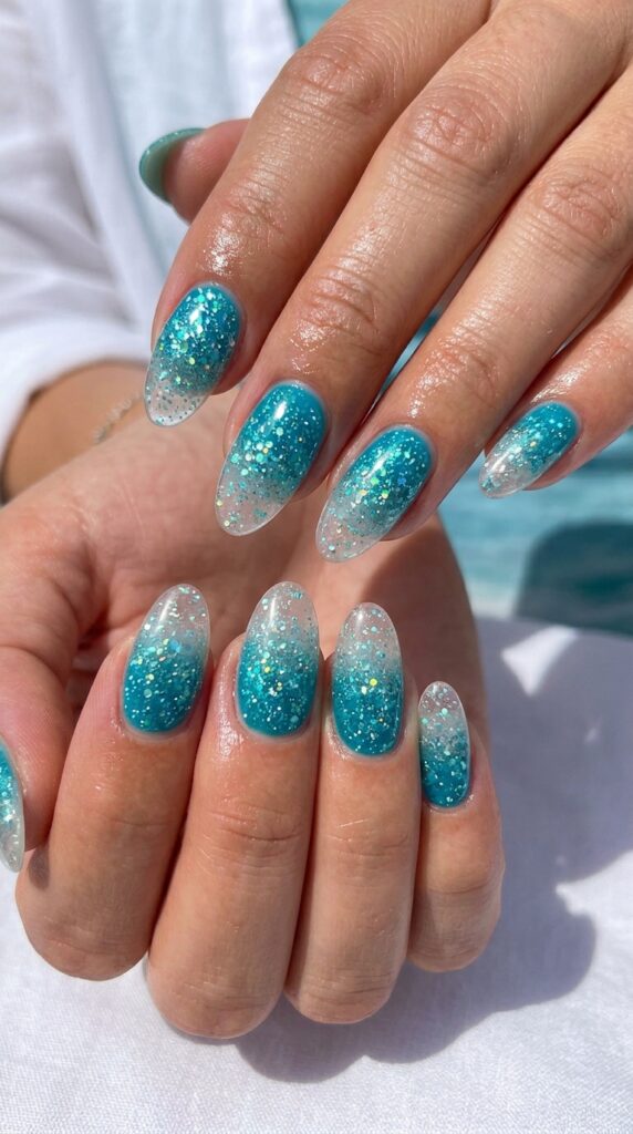Hands with turquoise glitter gradient showing transition from bright saturated turquoise at base to lighter sparkling turquoise at tips for ocean-inspired summer manicure